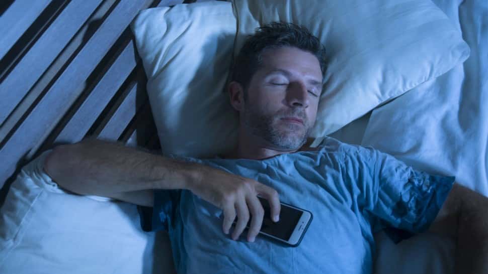 Obrazek Jak lepiej spać dzięki ustawieniom iPhone'a i kilku poprawkom | man-sleeping-smartphone-min-DzTechs