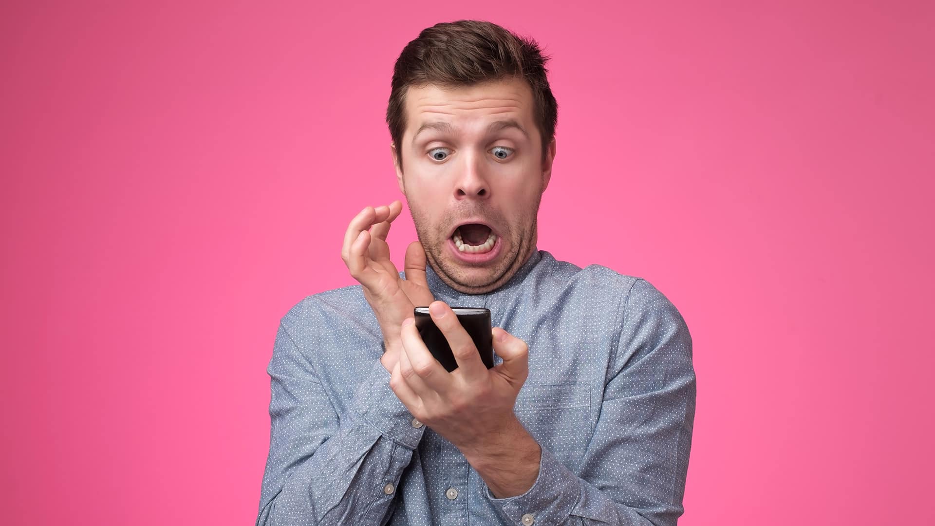 Uomo che guarda spaventato un telefono, con uno sfondo rosa