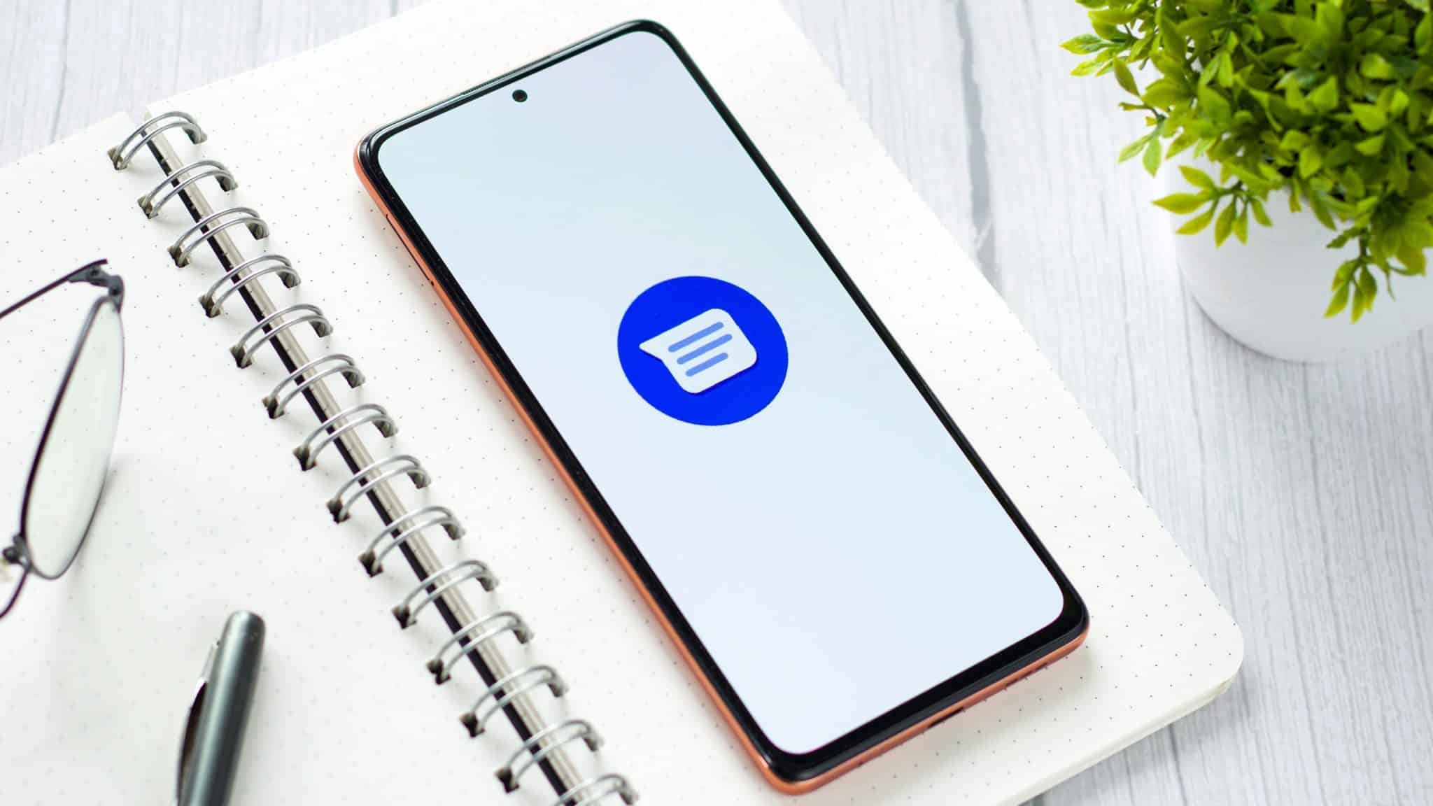 Telefon położony na notatniku, na którym widnieje logo Google Messages.