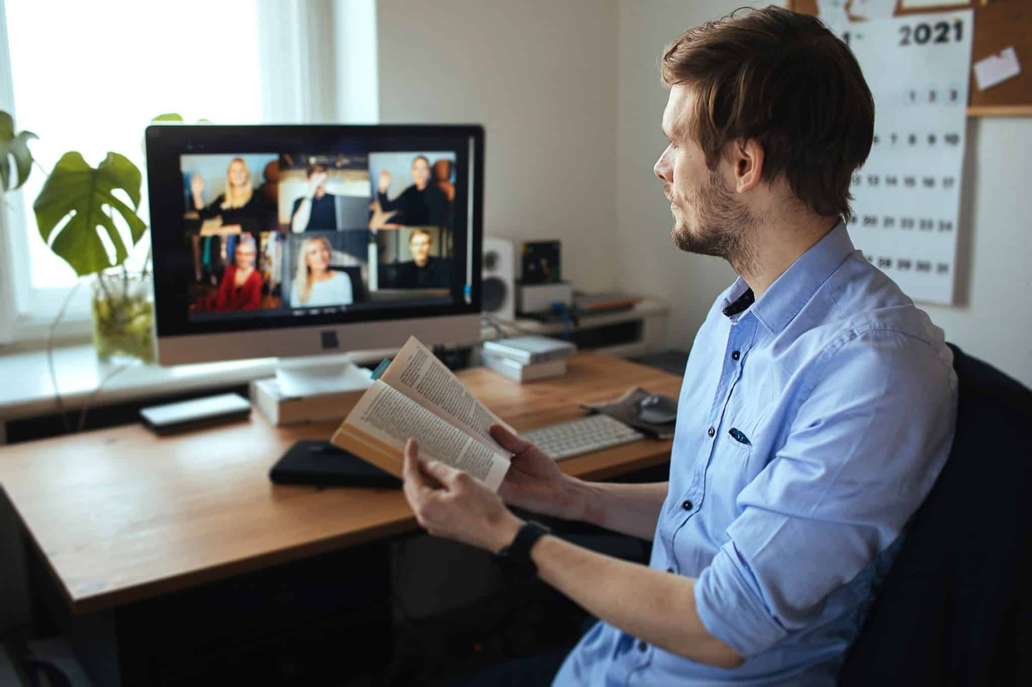 Mężczyzna czyta książkę w ramach internetowego klubu książki za pośrednictwem połączenia wideo.