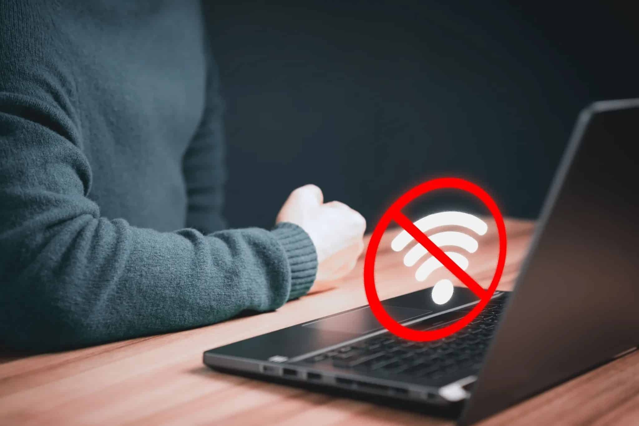 筆記型電腦上方顯示 Wi-Fi 斷開連接的圖標,桌子上有人將手臂放在筆記型電腦上