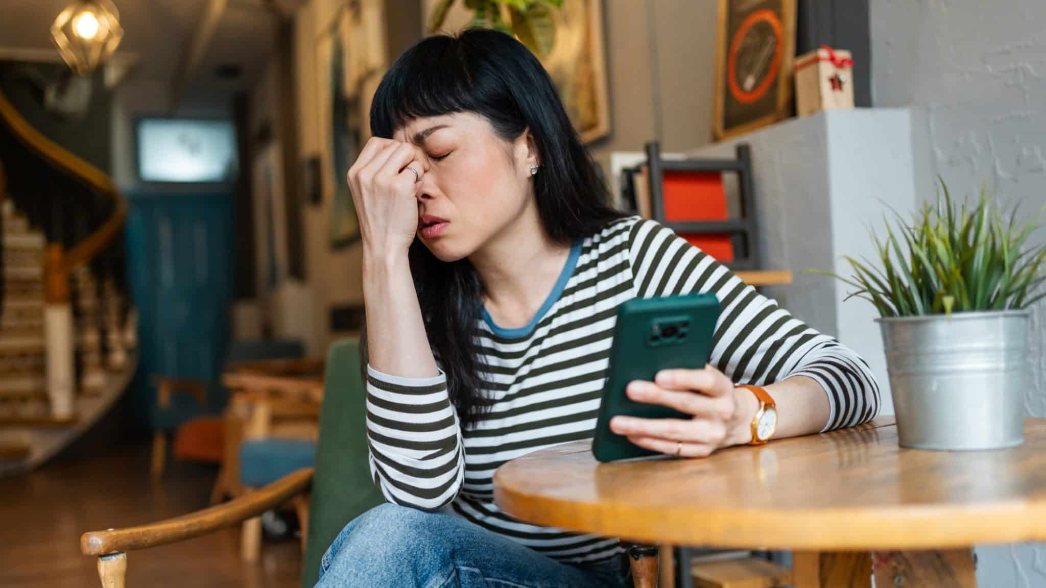 امرأة تحمل هاتفًا ذكيًا وتبدو محبطة