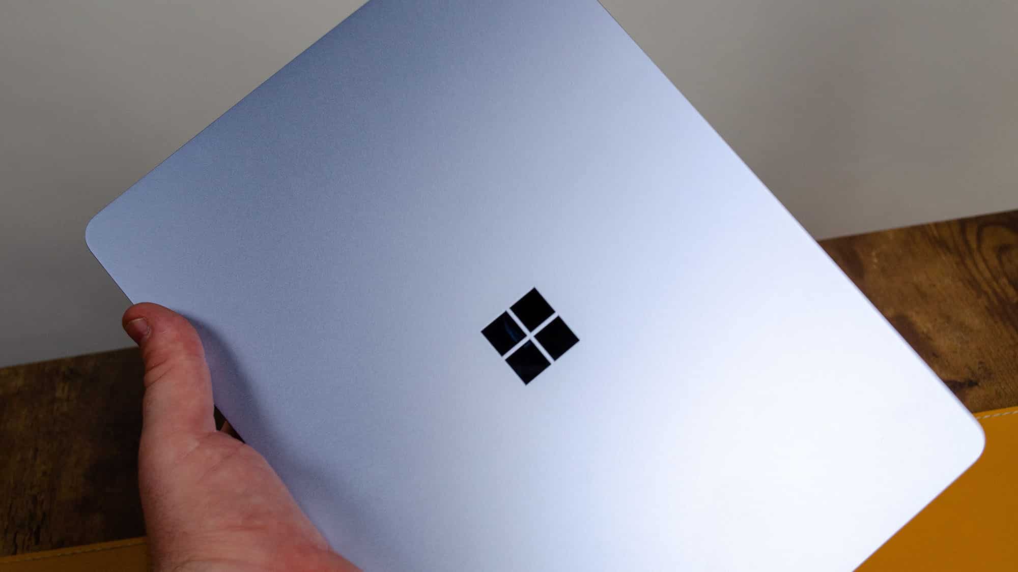 La mano de un hombre sosteniendo una computadora portátil Microsoft Surface de 13 pulgadas