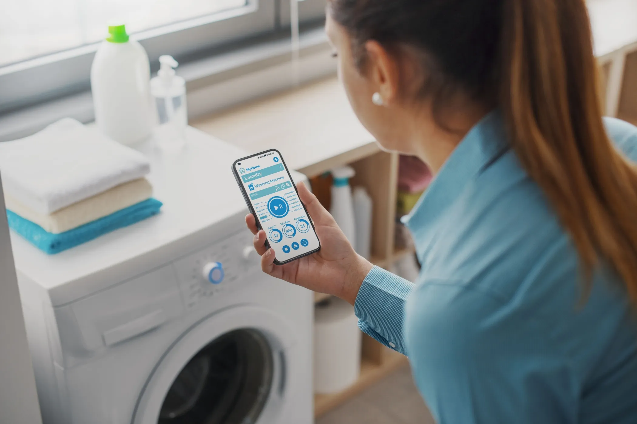 Eine Frau, die mit einem Smartphone eine Waschmaschine bedient