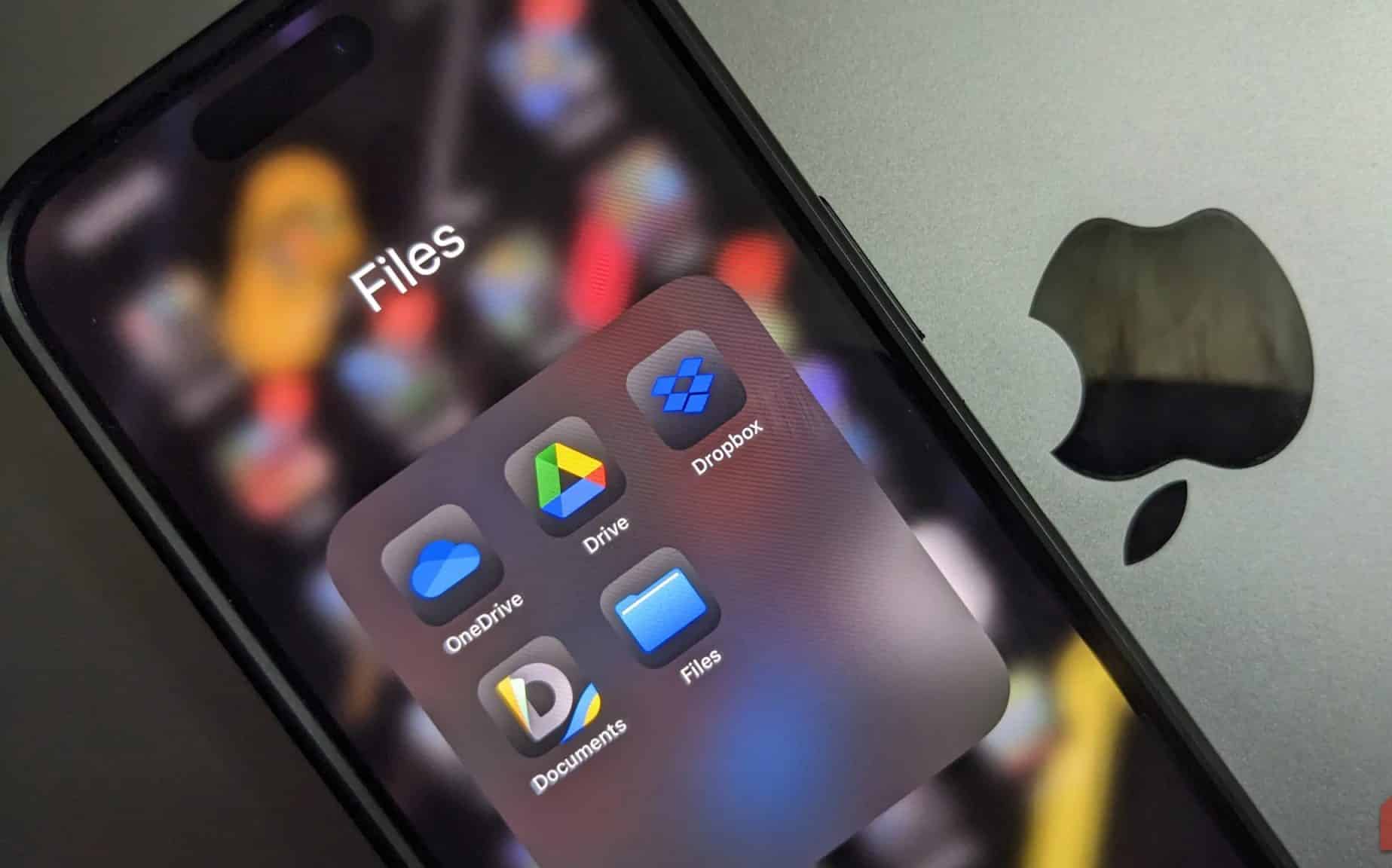 Der Ordner mit den Cloud-Speicher-Apps auf einem iPhone, das über einem MacBook mit dem Apple-Logo platziert ist
