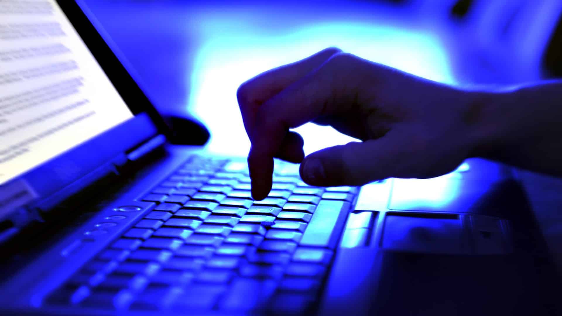 Ένα άτομο πληκτρολογεί σε ένα φορητό υπολογιστή, λουσμένο στο μπλε φως.