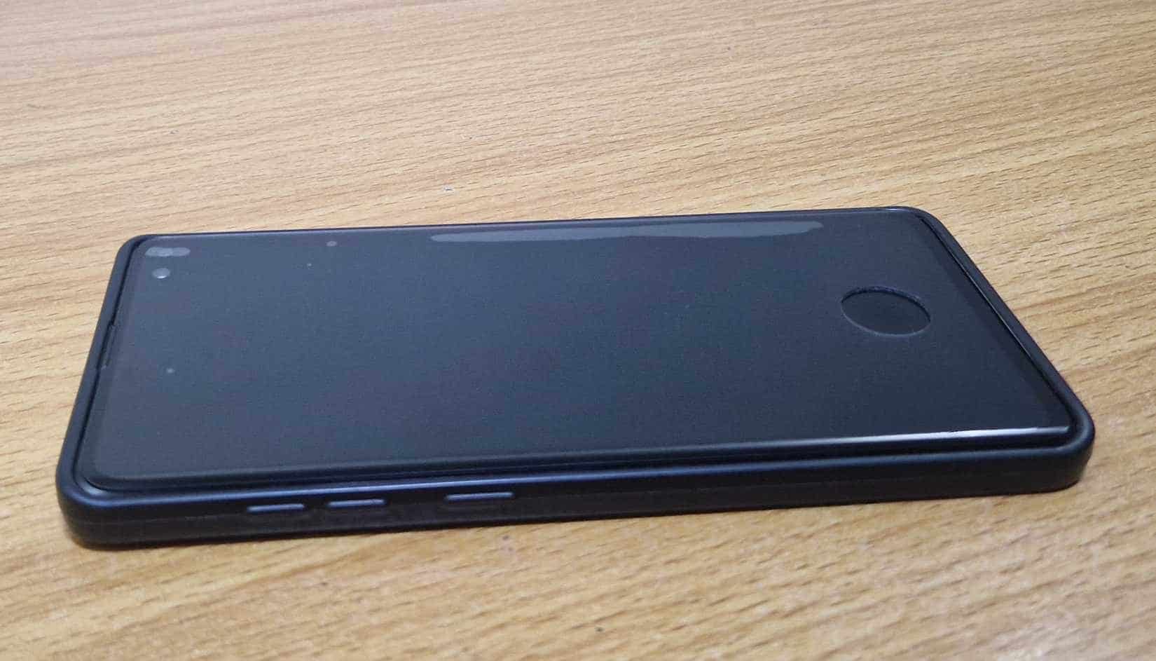 Folia ochronna na ekran z otworem na skaner linii papilarnych na górze telefonu Samsung położonego na stole.