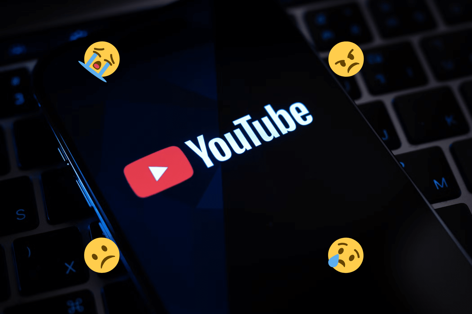 Uno smartphone mostra sullo schermo il logo di YouTube, circondato da emoji tristi e arrabbiate.